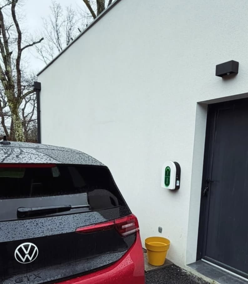 Borne de recharge murale à côté d'une voiture électrique garée devant une maison